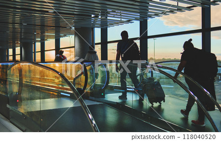 View on the aiport window with woman walking with suitcase at the departure hall during the sunset. Wide angle view with copy space. 118040520