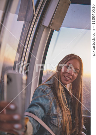 Young tourist sitting on the cableway in Caracas enjoying a photo taken on her smartphone. Bright sky, clouds and mountains. Selective focus 118040530