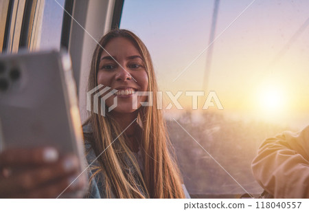Young tourist sitting on the cableway in Caracas enjoying a photo taken on her smartphone. Bright sky, clouds and mountains. Selective focus 118040557