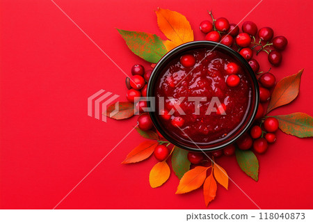 Bowl of cranberry sauce with fresh cranberries and autumn leaves on red background. Concept of holiday food Bowl of cranberry sauce with fresh cranberries and autumn leaves on red background. Concept of holiday food 118040873