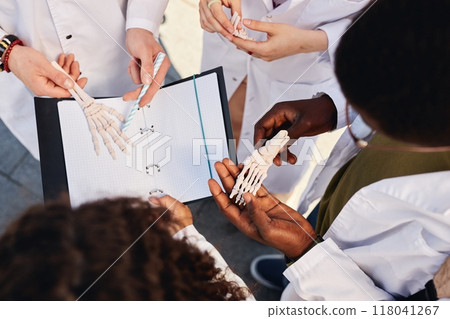 Top view of foot skeleton model in hands of African American medical student examining bones while standing in circle with classmates outdoors, copy space 118041267