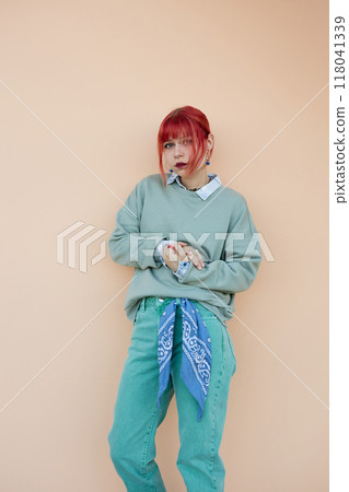 Vertical portrait of teenage girl with vibrant hair color dressed in pastel blue sweater and jeans styled with kerchief. Female student posing in shy way against pink wall, copy space Vertical portrait of teenage girl with vibrant hair color dressed in pastel blue sweater and jeans styled with kerchief. Female student posing in shy way against pink wall, copy space 118041339