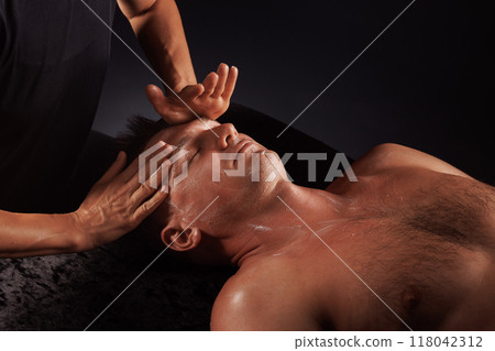 Female masseur doing facial massage to man lying on massage table.on dark uniform background, facial massage concept 118042312