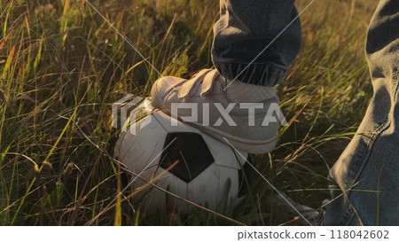 Child foot in field kicks ball playing football. Close up foot of teenage boy kid with soccer ball. Child kid at sunset in field kicking ball playing football alone enjoying football soccer game. Child foot in field kicks ball playing football. Close up foot of teenage boy kid with soccer ball. Child kid at sunset in field kicking ball playing football alone enjoying football soccer game. 118042602