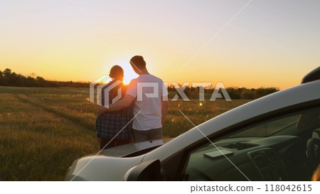 Married family couple in love hugging at sunset by car, romantically spending quiet time together, relaxing outside car. Husband and wife, spouses hugging, standing in field by car. Road trip, travel Married family couple in love hugging at sunset by car, romantically spending quiet time together, relaxing outside car. Husband and wife, spouses hugging, standing in field by car. Road trip, travel 118042615