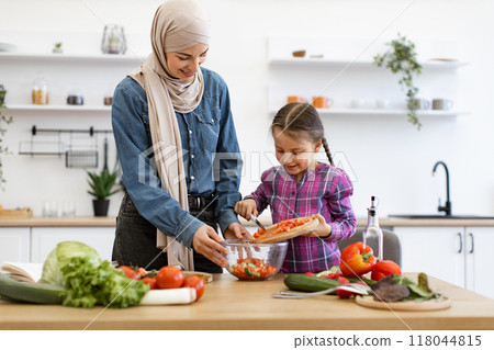 Muslim mother and daughter preparing fresh vegetable salad together 118044815