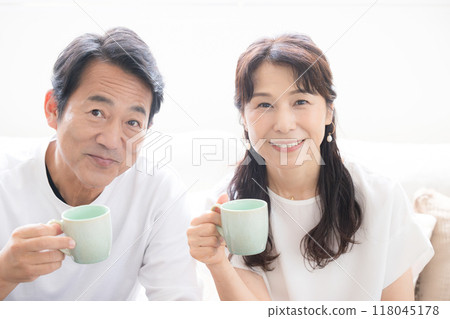 Close-up of a couple in their 50s in the backlight, looking at the camera, holding drinks 118045178