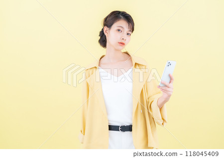 年輕女子看著黃色背景的智慧型手機 118045409