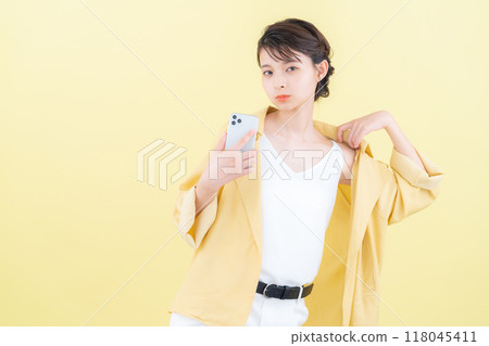 年輕女子看著黃色背景的智慧型手機 118045411