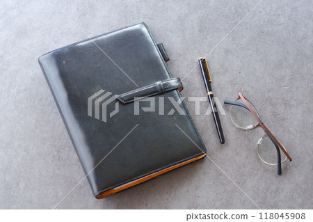 A black leather organizer, pen, and glasses A black leather organizer, pen, and glasses 118045908