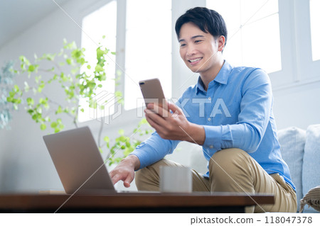 A man operating a smartphone while looking at a computer A man operating a smartphone while looking at a computer 118047378