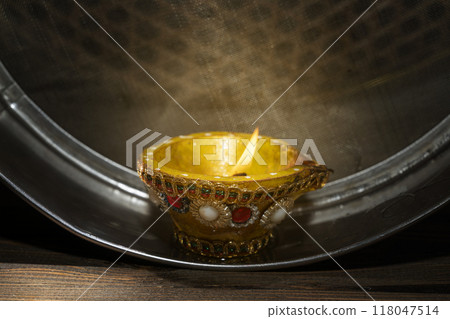 Diya oil lamp on the sieve. The candle is lit and the light is shining through the mesh 118047514