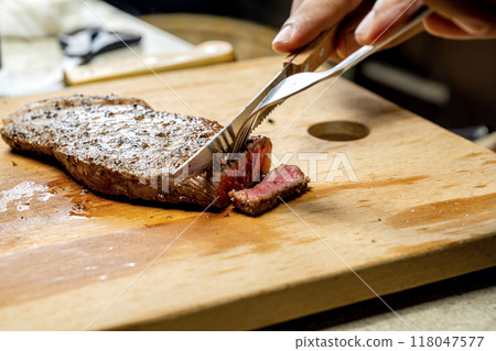 A person is cutting a piece of picanha meat with a knife and fork A person is cutting a piece of picanha meat with a knife and fork 118047577