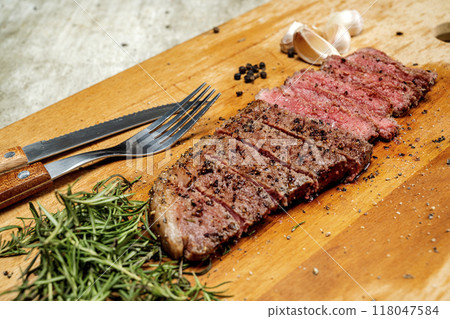 A piece of picanha meat is cut and sitting on a wooden cutting board with a fork and knife A piece of picanha meat is cut and sitting on a wooden cutting board with a fork and knife 118047584