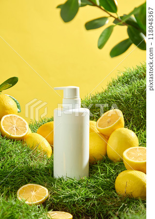 Advertising scene for natural cosmetics rich in vitamin C. Mockup cosmetic bottle displayed on green grass with fresh lemons and lemon slices. Unlabeled bottle for design 118048367