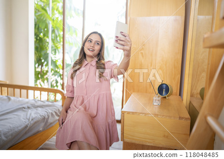 An Indonesian woman in a pink dress is taking a selfie with her cell phone 118048485