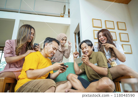 A group of Indonesian people are sitting on a couch and using their cell phones to play games A group of Indonesian people are sitting on a couch and using their cell phones to play games 118048590