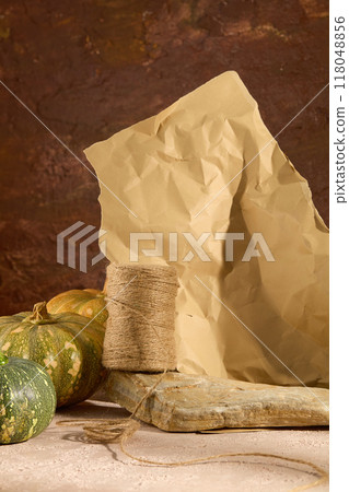 Minimalist creative background for products presentation with Autumn concept. Small rope rolls on stone decorated with green pumpkins and crumpled piece of paper on brown background Minimalist creative background for products presentation with Autumn concept. Small rope rolls on stone decorated with green pumpkins and crumpled piece of paper on brown background 118048856