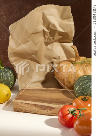 Promotional photo with creative autumn concept. Fresh pumpkins and tomatoes decorate a wooden platform and a piece of crumpled paper on brown. Blank space for design Promotional photo with creative autumn concept. Fresh pumpkins and tomatoes decorate a wooden platform and a piece of crumpled paper on brown. Blank space for design 118048872