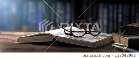 Open book and glasses on an antique wooden table 118048998