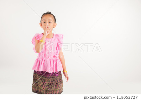 Portrait Thailand kid girl smiling traditional Thai dress costume making finger on lips mouth silent quiet gesture, studio isolated white background, kindergarten child marking silence for stop quiet 118052727