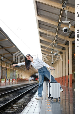 A woman is standing on a train platform with her luggage 118052975