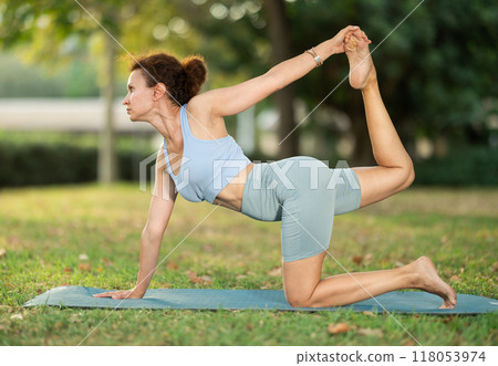 Woman doing yoga with wooden blocks on mat early morning outdoors 118053974