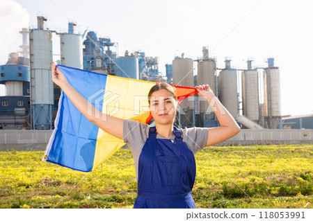 Happy young woman worker with flag of Romania against background of factory Happy young woman worker with flag of Romania against background of factory 118053991
