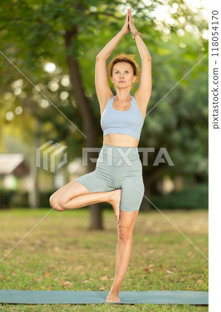 Focused female yoga practitioner performing Garudasana in garden Focused female yoga practitioner performing Garudasana in garden 118054170