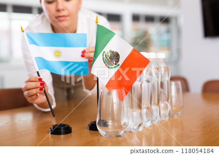 Female secretary places flags of the Mexico and Argentina flag on the table before negotiations of top political figures 118054184