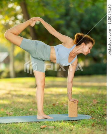 Woman doing yoga with wooden blocks on mat early morning outdoors 118054186
