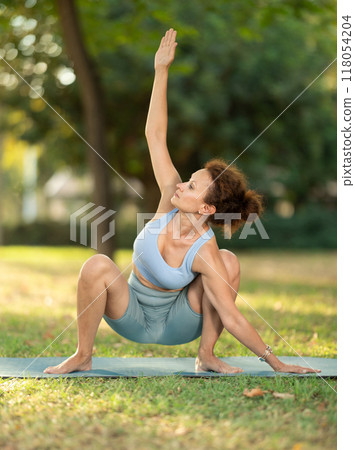 Woman in frog pose doing yoga in park. Healthy lifestyle concept Woman in frog pose doing yoga in park. Healthy lifestyle concept 118054204