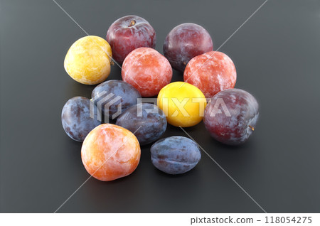 Assortment of colorful plums on a dark background, displaying a variety of fresh, ripe fruit 118054275