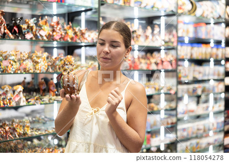 Female tourist happily chooses souvenir figurine of an eagle owl in Spanish souvenir shop 118054278