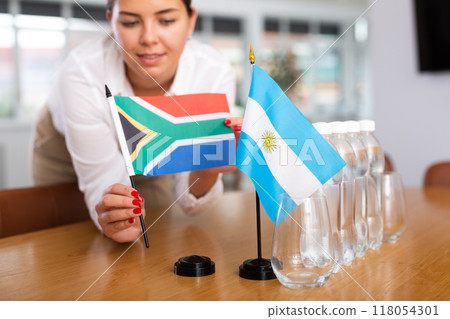 Preparing for business presentation - secretary places flags of Argentina and South Africa on negotiating table 118054301