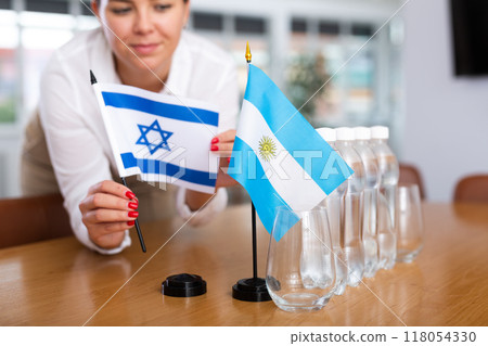 Unrecognizable girl sets midget flags of Argentina and Israel before international negotiations 118054330