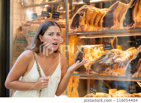 Outraged woman customer stands near shop window with dried beef ribs 118054484