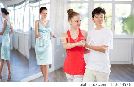 Dance lesson - teacher teaches teenage girl and boy to dance tango in studio Dance lesson - teacher teaches teenage girl and boy to dance tango in studio 118054526