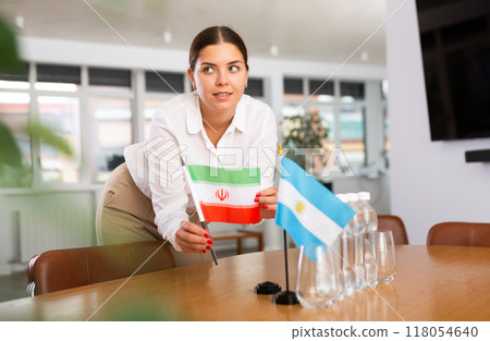 Employee of delegation prepares negotiating table - sets up flag of Argentina and Iran 118054640