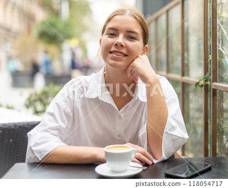 Portrait of young female at table in a cafe, drinking coffee from cup 118054717