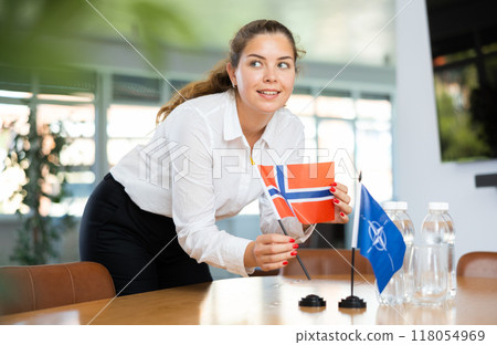 Young female secretary preparing room for international negotiations between nato and norway Young female secretary preparing room for international negotiations between nato and norway 118054969