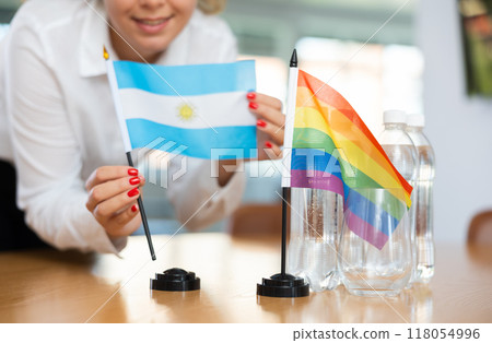 Young woman putting Argentina and LGBT flags on table in office 118054996