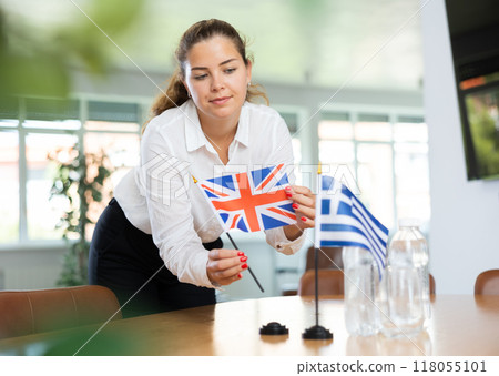 Young lady sets miniatures of flags of Greece and Great Britain before international negotiations 118055101