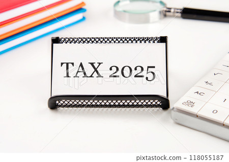 Conceptual tax 2025 symbol. Copy space. Tax 2025 words written on a business card in a composition with a magnifying glass, notebooks, a calculator on a white background 118055187
