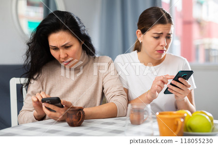 Two disappointed women using phone at home 118055230