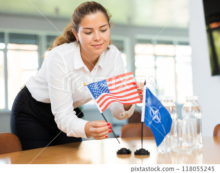 Female secretary places flags of the NATO (OTAN) and USA on the table before negotiations of top political figures Female secretary places flags of the NATO (OTAN) and USA on the table before negotiations of top political figures 118055245