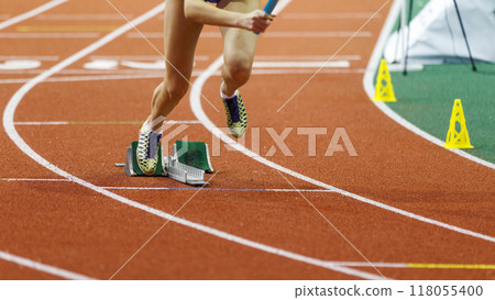 Athlete in sprinting shoes launches off the starting blocks during a competitive track race on an indoor arena surface Athlete in sprinting shoes launches off the starting blocks during a competitive track race on an indoor arena surface 118055400