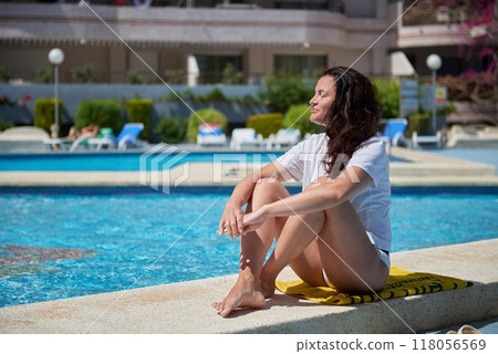 Mediterranean Bliss: Young Woman Relaxing Poolside at Luxurious Resort Under Swaying Palm Trees on Summer Vacation. Serene Summer Getaway: 30-Year-Old Female Sunbathing by Infinity Pool in Idyllic Mediterranean Bliss: Young Woman Relaxing Poolside at Luxurious Resort Under Swaying Palm Trees on Summer Vacation. Serene Summer Getaway: 30-Year-Old Female Sunbathing by Infinity Pool in Idyllic 118056569