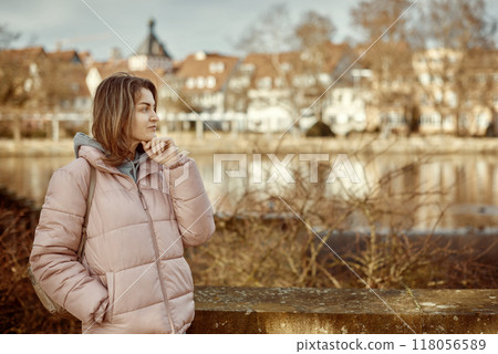 Young beautiful pretty tourist girl in warm hat and coat with backpack walking at cold autumn in Europe city enjoying her travel in Bietigheim-Bissingen, Deutschland. Outdoor portrait of young tourist Young beautiful pretty tourist girl in warm hat and coat with backpack walking at cold autumn in Europe city enjoying her travel in Bietigheim-Bissingen, Deutschland. Outdoor portrait of young tourist 118056589