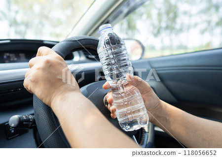 Asian woman driver holding bottle for drink water while driving a car. Plastic hot water bottle cause fire. Asian woman driver holding bottle for drink water while driving a car. Plastic hot water bottle cause fire. 118056652